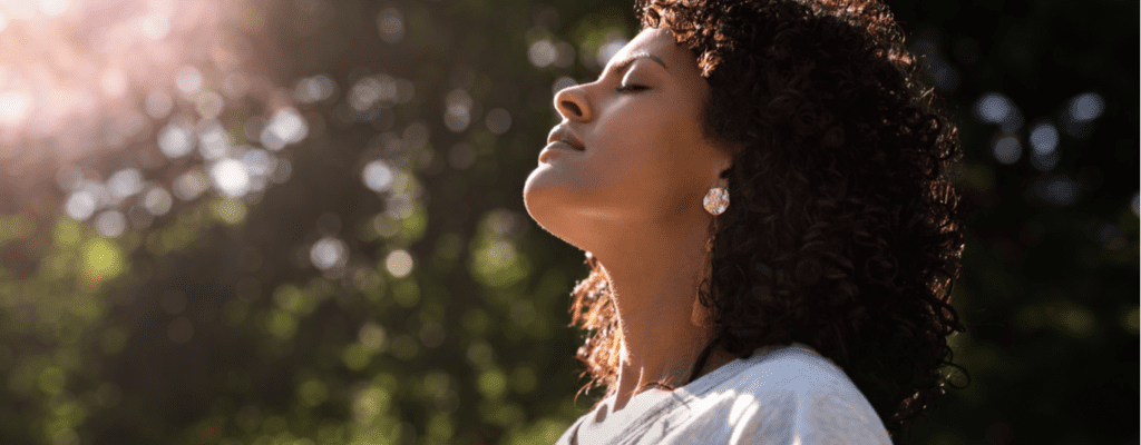 A young woman stands outside with her eyes closed basking in the sun.