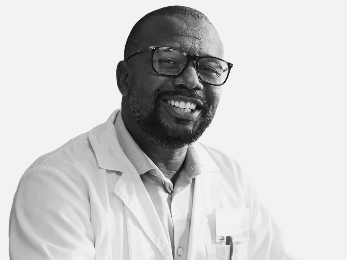 A middle aged African American man in a white lab coat and dark glasses smiles.