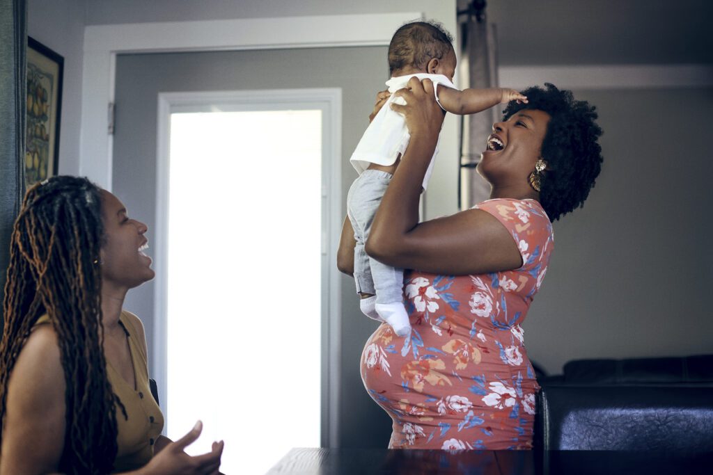 Maya Jackson, pregnant, smiles holding a tolder in the air