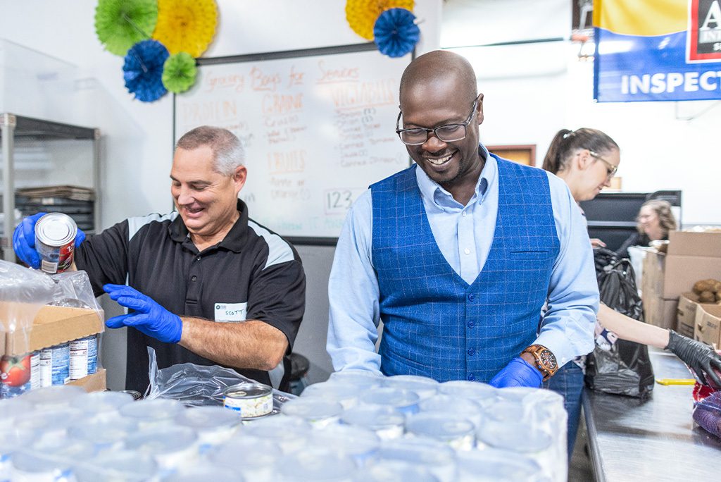Two men smile while sorting canned goods